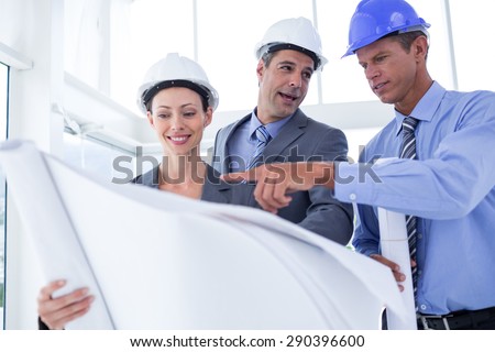 Businessmen and a woman with hard hats and holding blueprint in the office