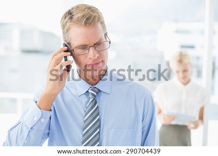 Businessman having a phone call with colleague in background in an office