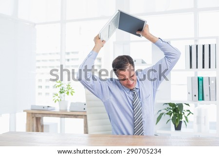 Irritated businessman trying to broke his laptop in his office