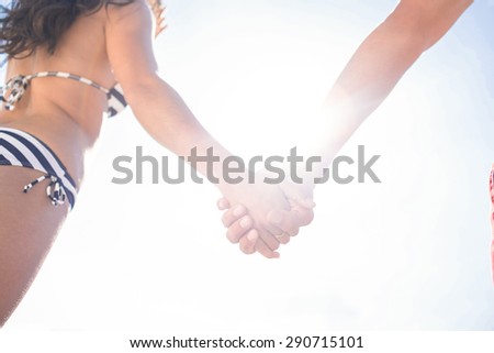 Rear view of couple holding hands at the beach on a sunny day
