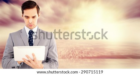 Businessman holding a tablet computer against room with large window looking on city