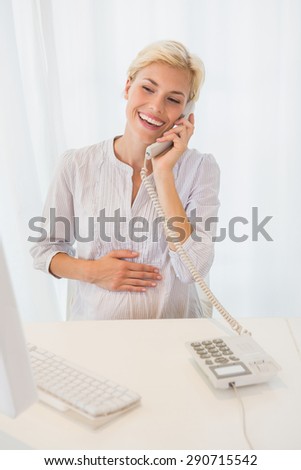 Smiling blonde woman using computer and phoning in the office