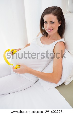 Happy pregnancy putting headphone on his belly at home in bedroom
