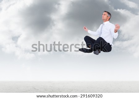 Peaceful businessman sitting in lotus pose against cloudy sky background