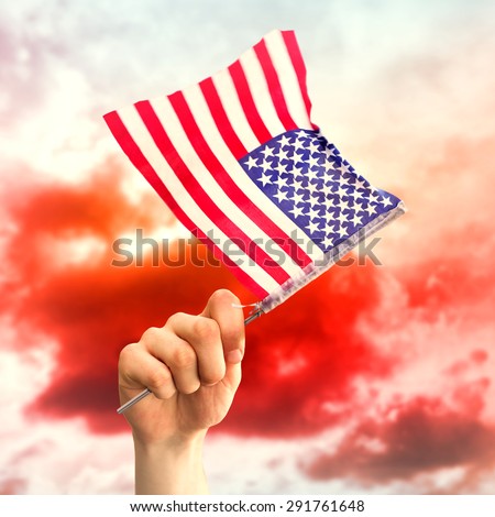 Hand waving american flag against green grass under red cloudy sky