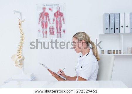 Doctor writing on clipboard at her desk in medical office