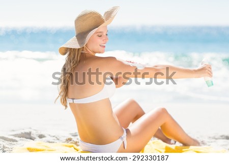 Pretty blonde woman spreading sun tan lotion on her arms at the beach