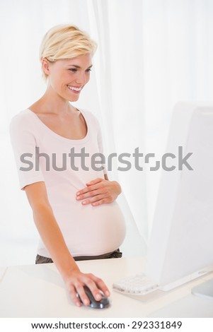 Smiling of a blonde pregnant using computer in the office