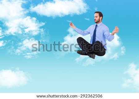 Businessman in suit sitting in lotus pose against blue sky