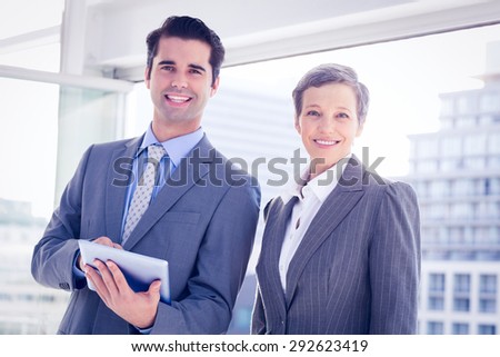 Business colleagues smiling at camera and holding tablet in the office