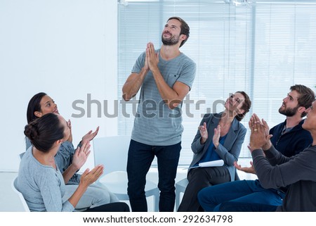 Rehab group applauding delighted man standing up at therapy session