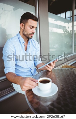Attentive businessman using a tablet while holding coffee cup outside the cafe