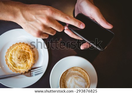 Close up view of pastry beside hands showing a smartphone
