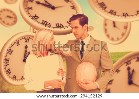 Architects with plans and hard hat looking at each other against green field under blue sky