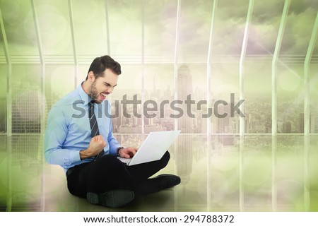 Cheering businessman sitting using his laptop against room with large window looking on city