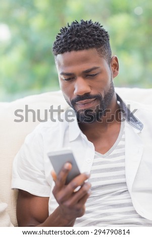 Handsome man using his smartphone at home in the living room
