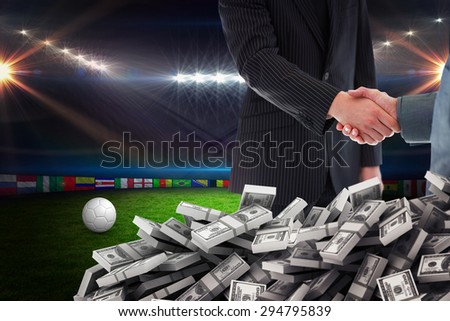 Business people shaking hands against football pitch with lights and flags