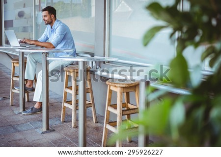 Distant view of a smiling businessman using his laptop outside a cafe