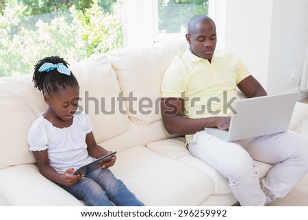 Happy father using laptop and her daughter using tablet on couch in living room