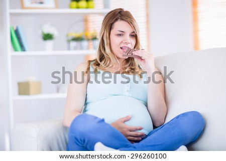 Pretty pregnant woman eating chocolate at home in the living room
