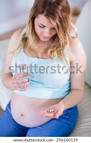 Pregnant woman taking a vitamin tablet at home in the living room