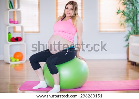 Pregnant woman looking at camera sitting on exercise ball in the living room