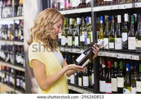 Smiling pretty blonde woman looking at a wine bottle in supermarket