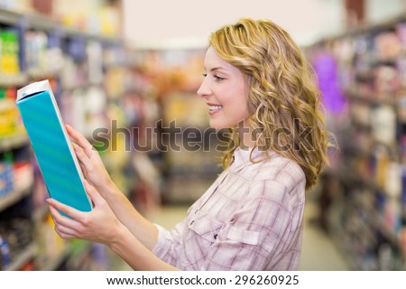 Side view of smiling pretty blonde woman reading a book in supermarket