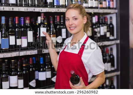 Portrait of a smiling blonde worker taking a wine bottle in supermarket