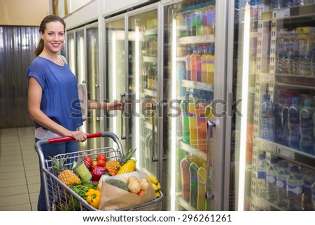 Pretty woman looking at camera and taking product on fridge at supermarket