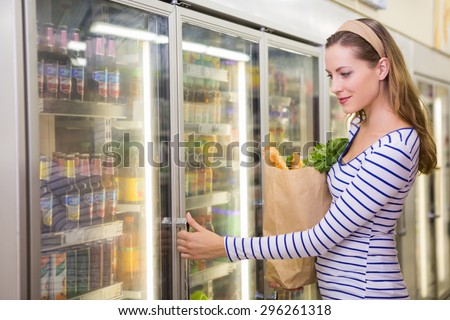 Pretty woman taking product on fridge at supermarket