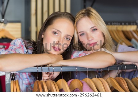Two serious female friends looking at camera in clothes store