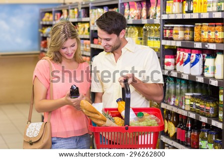 Smiling bright couple buying food products with shopping basket at supermarket