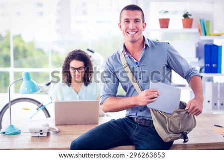 Creative businessman looking at the camera while tidying tablet in the bag