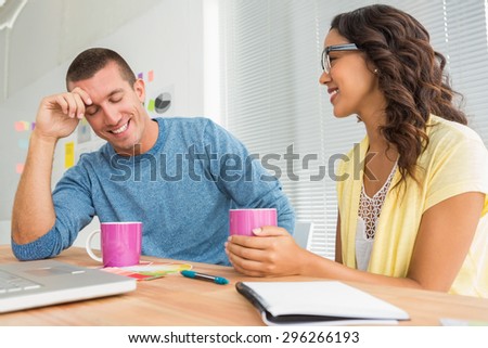 Smiling colleagues speaking together at desk in the office