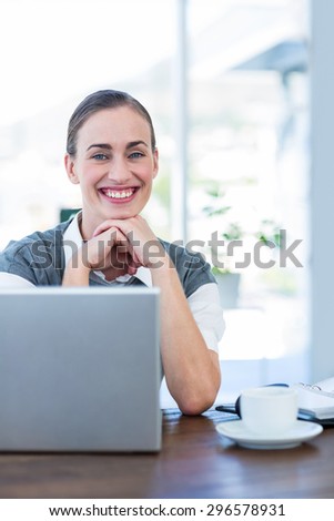 Happy businesswoman looking at camera behind laptop computer in office