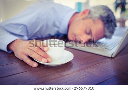 Businessman sleeping on laptop computer and touching coffee cup in office
