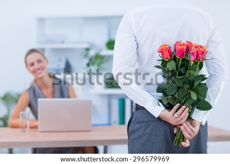 Businessman hiding flowers behind back for colleague in the office