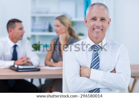 Happy businessman smiling at camera with colleagues behind in the office