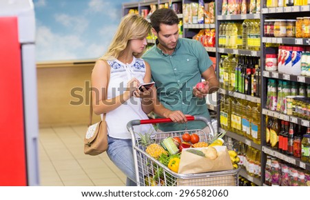 Bright couple buying food products and using notebook at supermarket