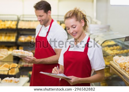 Two smiling colleagues writing on notepad in bakery