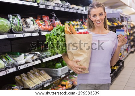 Pretty blonde woman holding bag and credit card in supermarket