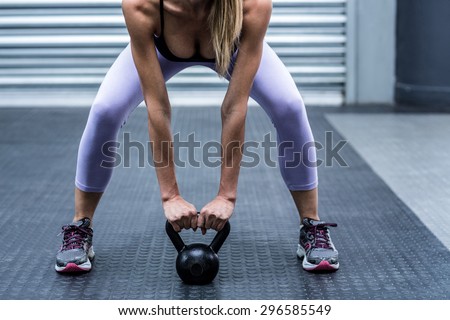Squatting muscular woman lifting kettlebells at the crossfit gym