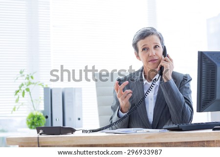 Serious businesswoman phoning and using computer at the office