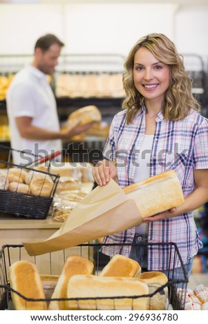 Portrait of a smiling blonde woman taking a bread on her paper bag in bakery