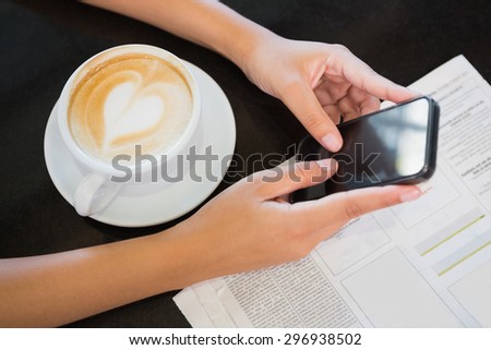 Coffee with a heart and hands holding a phone in the cafe