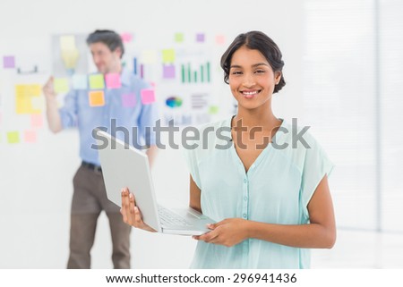 Smiling businesswoman presenting laptop screen with colleague behind her in the office