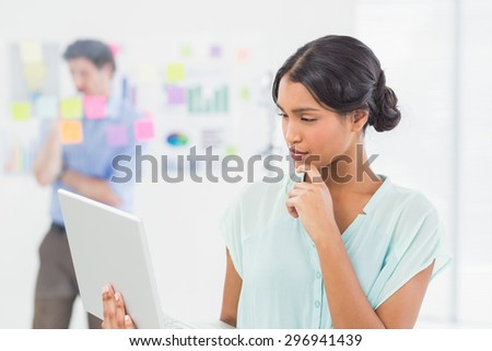 Businesswoman working on laptop screen with colleague behind her in the office