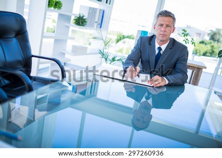 Businessman writing on clipboard and looking at camera in office