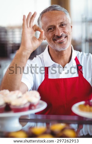Happy barista looking at camera and gesturing ok sign behind counter in the bakery